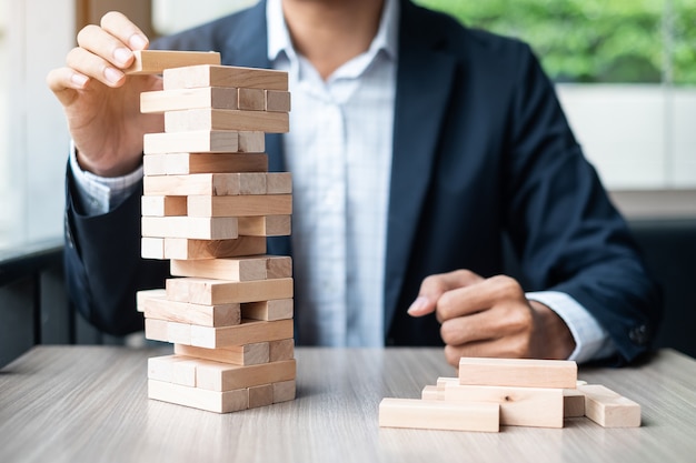 Businessman hand placing or pulling wooden block on the tower