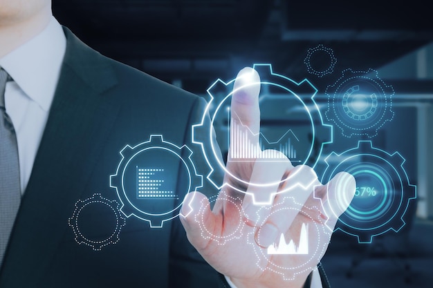 businessman hand pointing at glowing cogwheel and chart hologram on blurry office interior background business analytics and finance concept double exposure