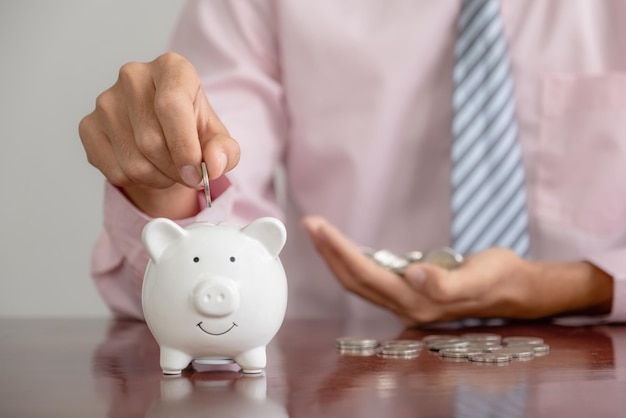 Businessman hand putting coin money into white piggy bank