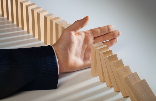 Businessman hand stop falling domino pieces