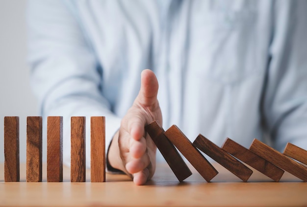 Businessman hand stop wooden block falling others block dominos\
for risk and crisis management concept