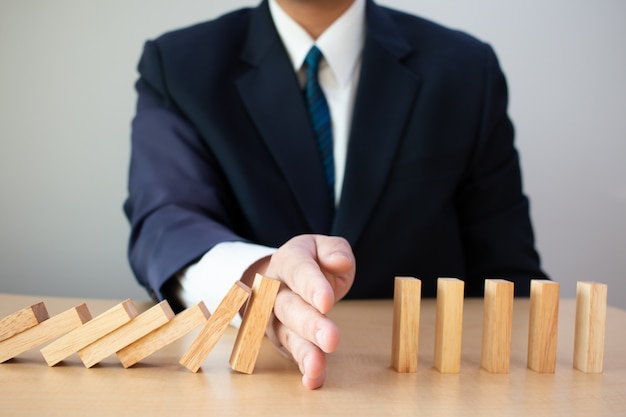 Businessman hand stopping falling wooden dominoes.business risk\
control concept.business risk planning and strategy.