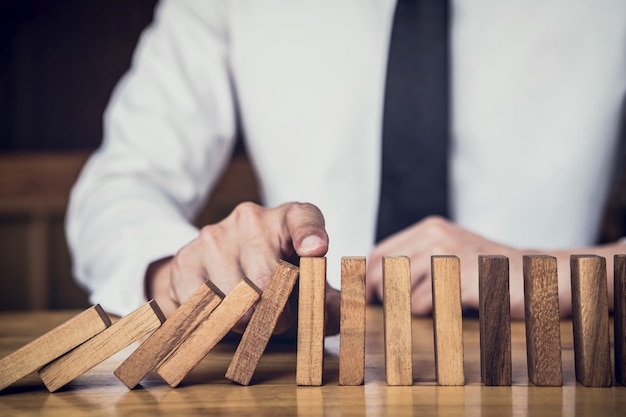 businessman hand Stopping Falling wooden Dominoes effect from continuous topple