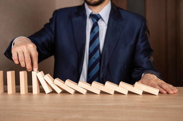 Mano dell'uomo d'affari che arresta l'effetto domino di legno di caduta dal continuo ribaltamento o rischio, strategia e concetto di intervento di successo per il business.