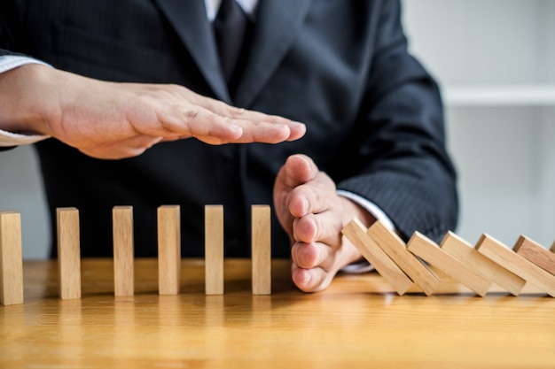 La mano dell'uomo d'affari che ferma l'effetto di legno di domino di caduta dal continuo ha rovesciato o rischia