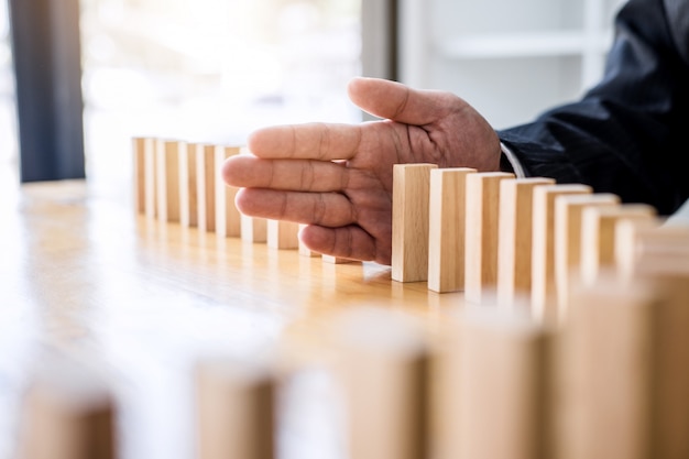 Businessman hand stopping falling wooden dominoes effect 