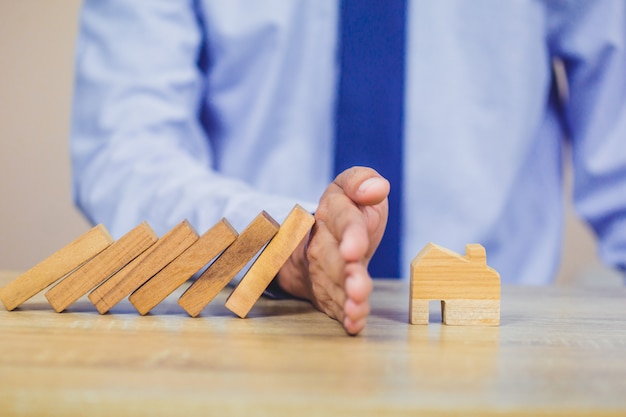 Photo businessman hand stopping risk the wooden blocks from falling on house.