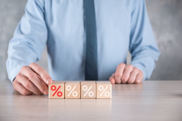 Businessman hand takes a wooden cube block depicting,shown the percentage symbol icon. Interest rate financial and mortgage rates concept.