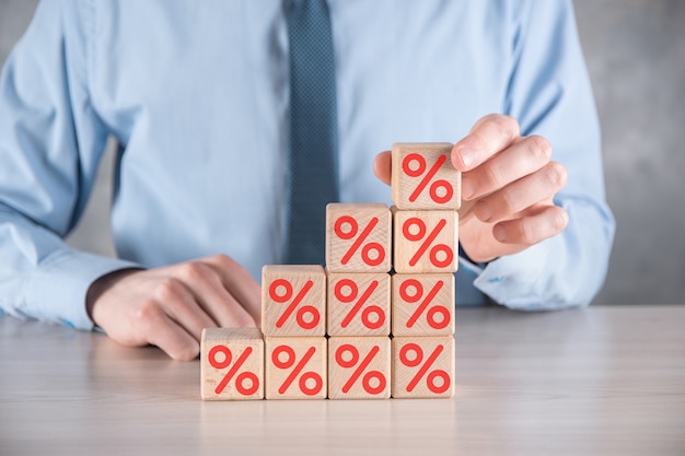 Businessman hand takes a wooden cube block depicting,shown the percentage symbol icon.