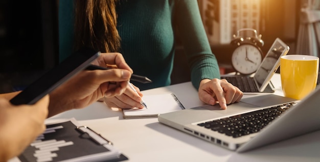 Mano dell'uomo d'affari che utilizza smartphone laptop e tablet con diagramma di rete sociale e due colleghi che discutono dei dati sulla scrivania come concetto al mattino lightxa