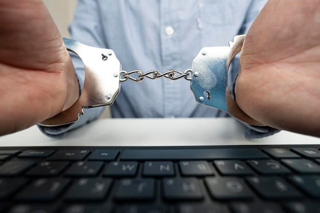 Photo businessman hand with handcuffs and computer laptop concept of crimes in cyberspace