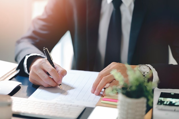 Businessman hand writing on paperwork while sitting at office desk in modern office.