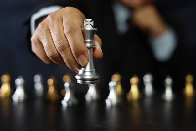 Businessman hands in black suite sitting and pointing chess king on vintage table