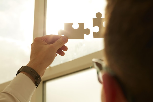 Businessman hands connecting puzzle pieces representing the merging of two companies or joint venture partnership Mergers and acquisition concept