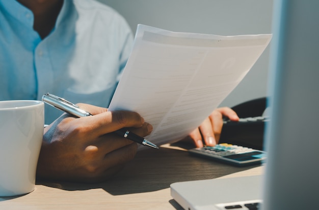 Businessman hands on a desk with coffee mugs and computers, holding pens and business documents. Online payments for businesses, finance, investments, and taxes