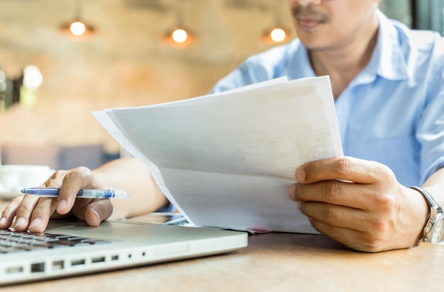 Businessman hands holding document paperwork and pen working on laptop.