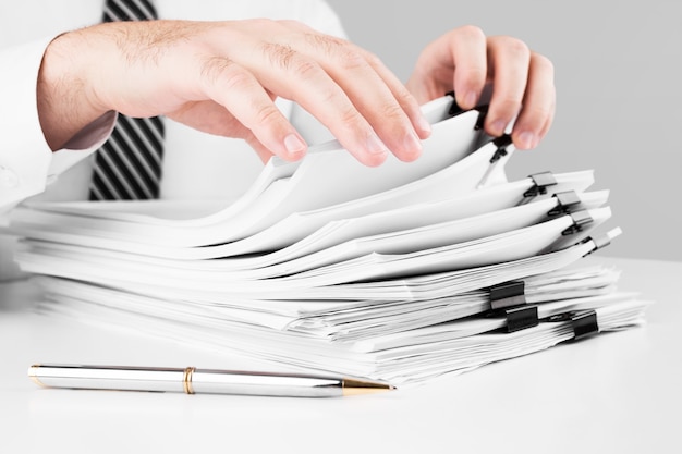 Businessman hands working in stacks of paper files for searching information, business and financial concept.