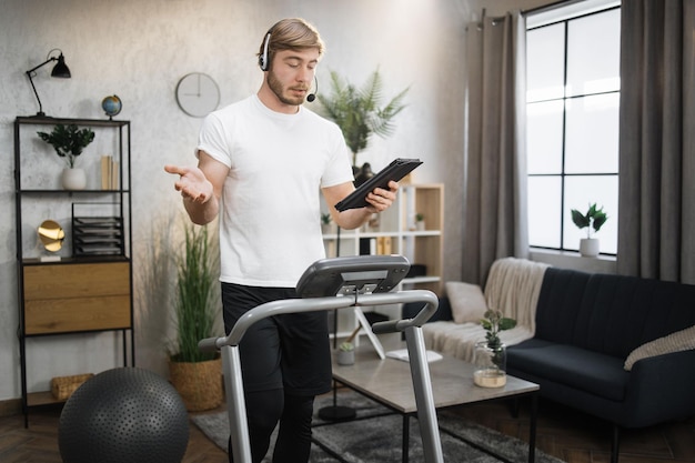 Businessman in headset working remote from home using digital tablet while having cardio workout