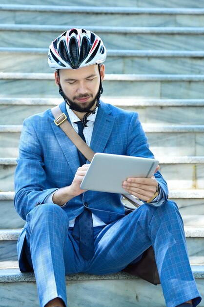 Businessman in helmet sitting on stairs and analyzes report on digital tablet