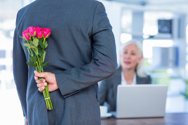 Businessman hiding flowers behind back for colleague