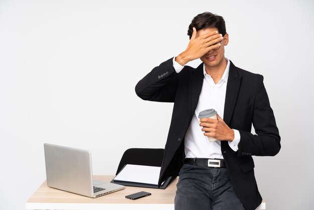 Businessman in his office over isolated wall white wall covering eyes by hands