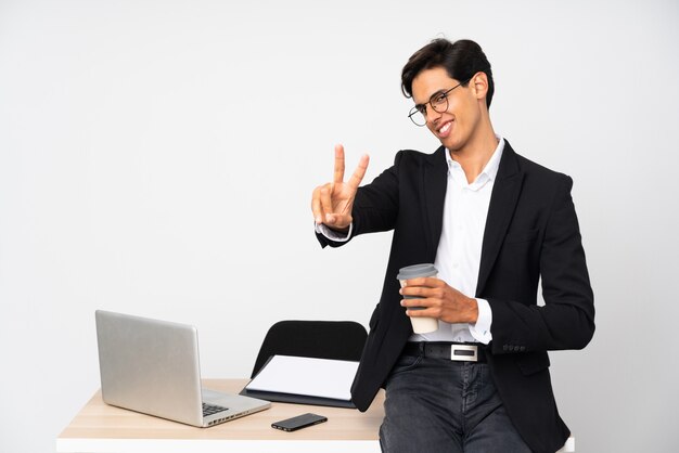 Businessman in his office over isolated wall white wall smiling and showing victory sign