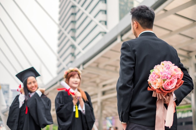 Бизнесмен держит, скрывая букет цветов для поздравления молодой женщины, получившей степень бакалавра
