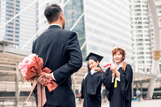 사업가는 젊은 여성의 학사 학위 졸업을 축하하기 위해 꽃다발을 숨기고 있다