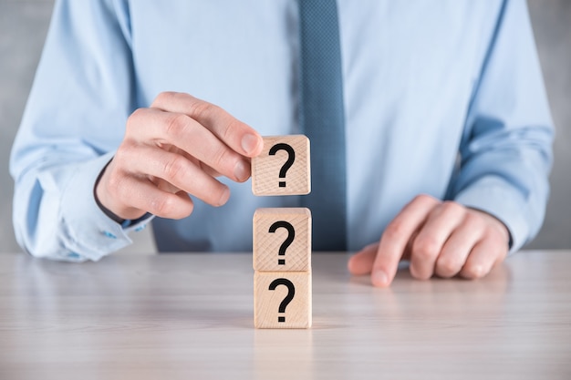 Businessman hold and put wooden cube block shape with question marks on grey table. Space for text.concept for confusion, question or solution.