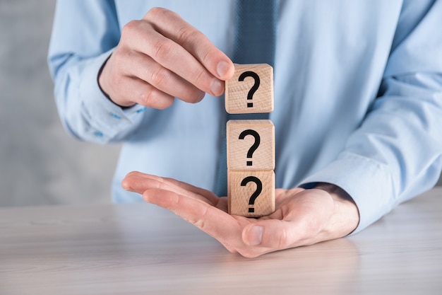 Businessman hold and put wooden cube block shape with question marks on grey table. Space for text.concept for confusion, question or solution.