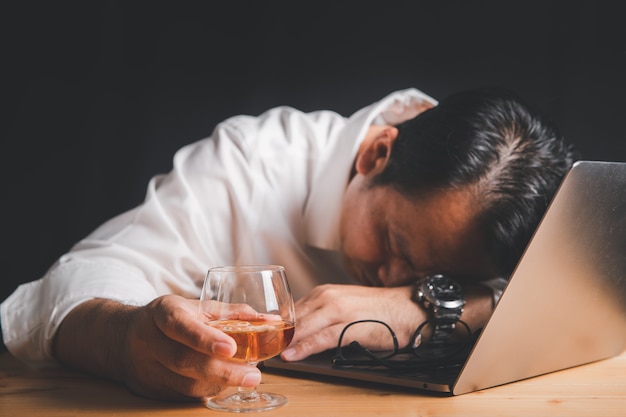 Imprenditore tenere il bicchiere di whisky e dormire sul computer portatile