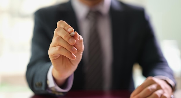 Businessman holding ballpoint pen in front of camera at work in office closeup