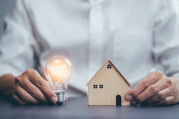 Businessman holding bright lights bulb and house model