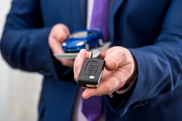 Businessman holding car key, toy car and money