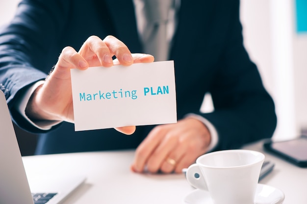 Businessman holding a card with marketing plan written on it. Close up