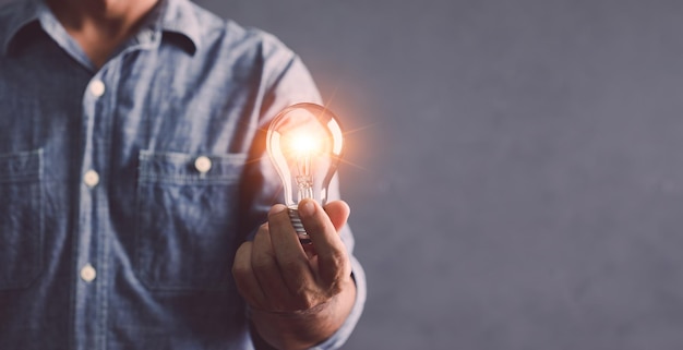 Businessman holding a clear light bulb with light effect on gray space wall background Concept of new ideas for work