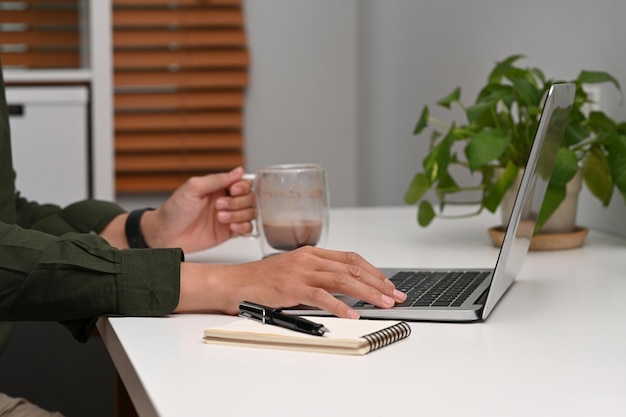 Businessman holding coffee cup and working with laptop computer home office