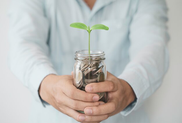 Бизнесмен, держащий монеты в копилке с растениями, инвестиционной прибылью и деньгами в виде дивидендов от концепции сбережений.
