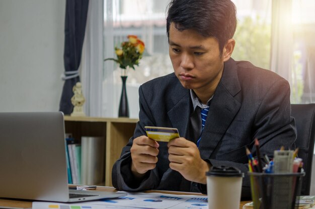 Businessman holding a credit card looking at documents graphs finances and economic investments at the computer with anxiety planning and online shopping with stress