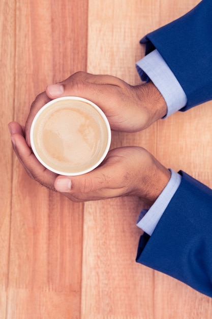 Businessman holding disposable coffee cup at wooden desk in office