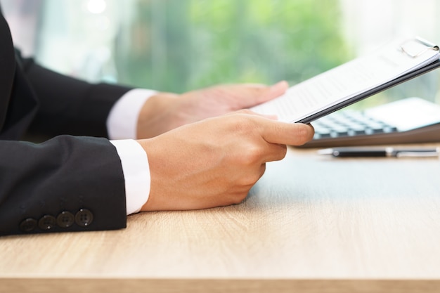 Businessman holding document with calculator on wooden desk.