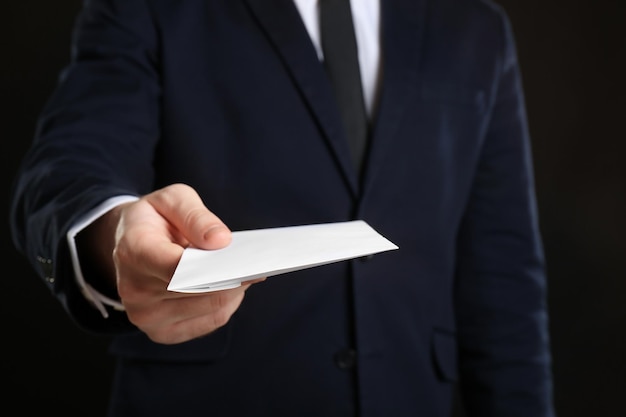 Businessman holding envelope with bribe on black background