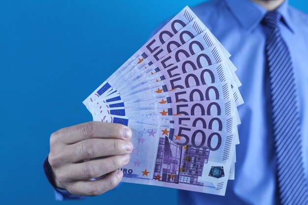 Businessman holding euro banknotes on blue background