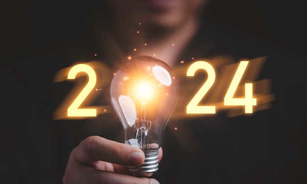 Uomo d'affari che tiene una lampadina incandescente con il numero 2024 per un'idea di pensiero creativo per iniziare un nuovo concetto di business