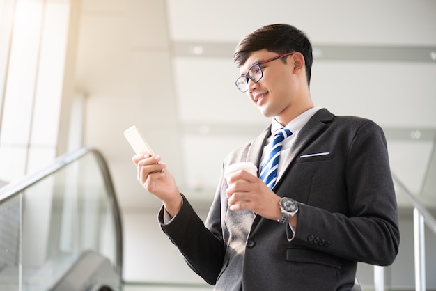 Businessman holding hot coffee cup and using his phone