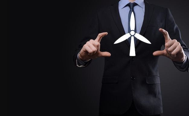 Бизнесмен держит икону ветряной мельницы, которая производит энергию окружающей среды Темный фон
