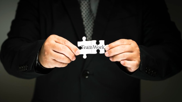 Businessman holding a jigsaw peice in hand. The letter word teamwork. Work as a team concept and working theory group coordination in the organization.