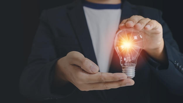 ライトフレアと電球を保持しているビジネスマン。創造的なアイデアの天才イノベーション知識が成功しました。シンボル思考の創造的な概念。