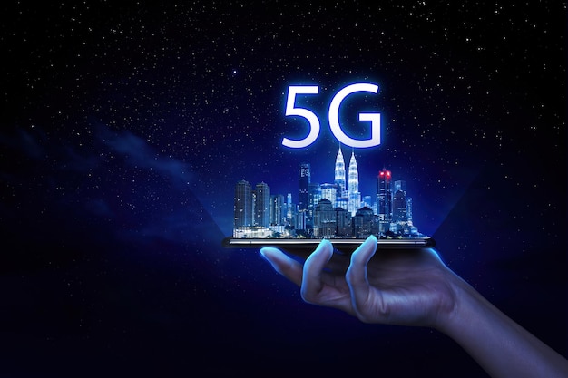 Бизнесмен держит мобильный телефон с городом Куала-Лумпур и текстом 5G на виртуальном экране на фоне ночных звезд