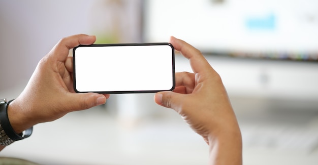 Businessman holding a mobile phone with white screen over the desk in the office